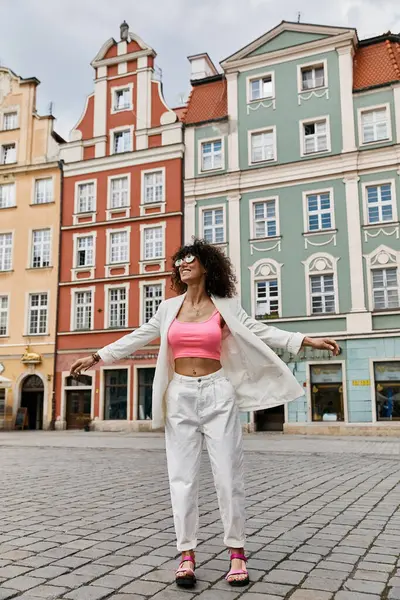 Eine stylische Frau in weißem Blazer und weißer Hose posiert vor bunten Gebäuden in Europa. — Stockfoto