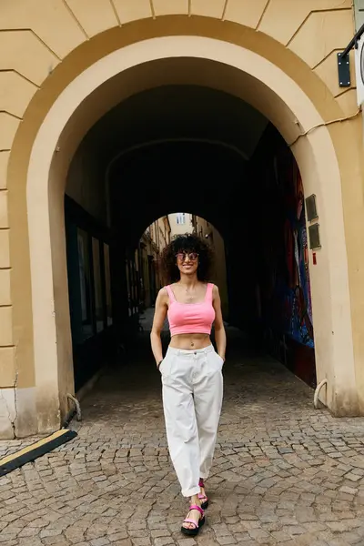 A woman in trendy attire walks under a stone archway during her European trip. — Stock Photo