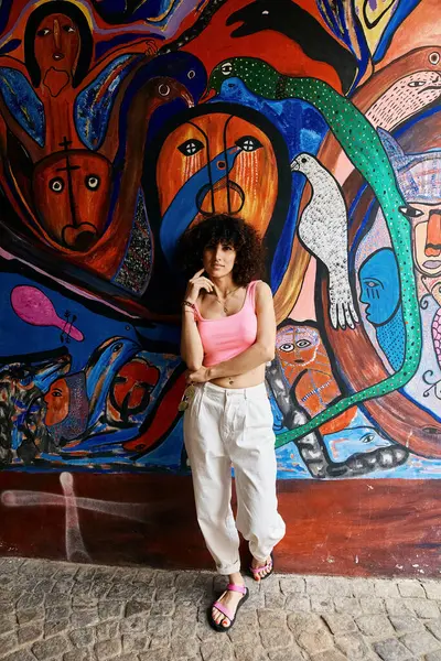 A woman in stylish attire stands against a vibrant, colorful mural in Europe. — Stock Photo