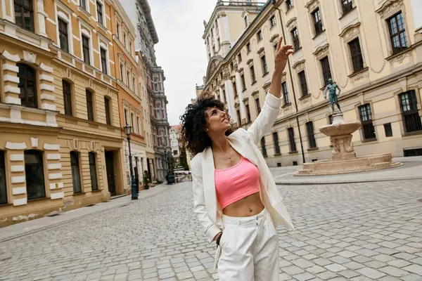 Una donna in blazer bianco e crop top rosa posa su una strada europea. — Foto stock