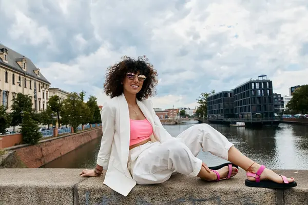 A stylish woman in white sits on a bridge overlooking a European canal. — Stock Photo