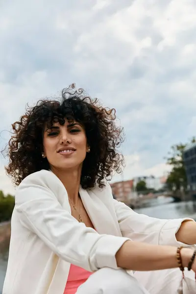A stylish woman with curly hair poses in a white blazer during a European trip. — Stock Photo