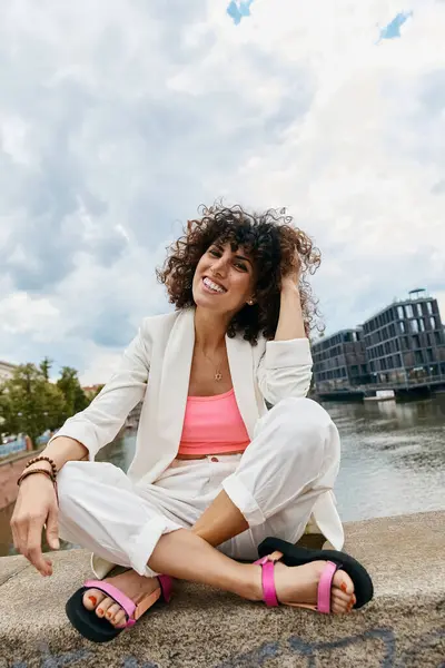 A stylish woman smiles while sitting by a canal in Europe. — Stock Photo
