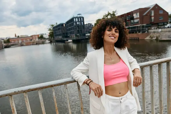 A woman in fashionable attire poses on a bridge overlooking a canal in a European city. — Stock Photo