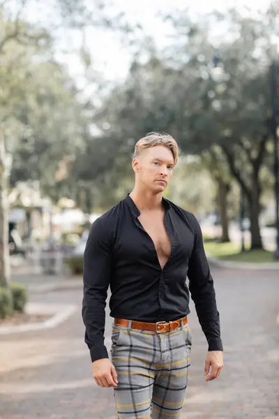 Un guapo hombre rubio camina por una calle en Orlando, Florida. Lleva una elegante camisa negra y pantalones a cuadros.. — Stock Photo