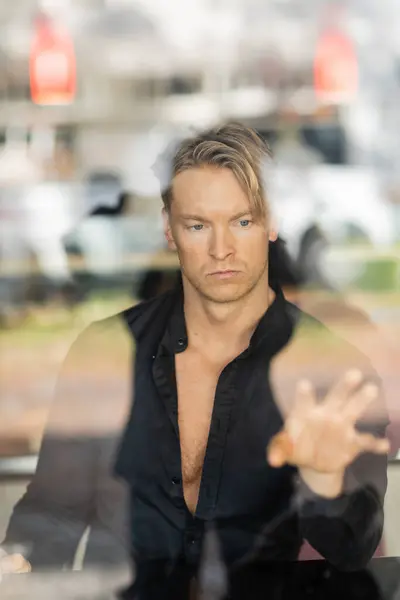 A handsome blonde man in a black button-down shirt is reflected in a window — Stock Photo