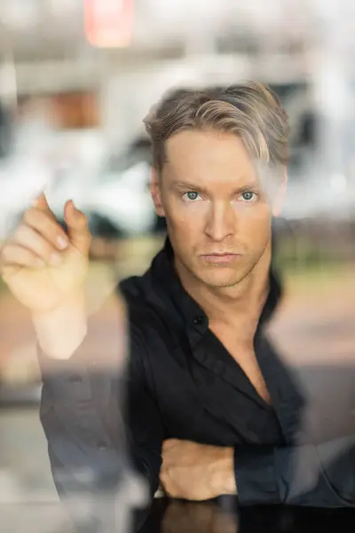 A handsome blonde man in stylish attire, viewed through a window reflection — Stock Photo