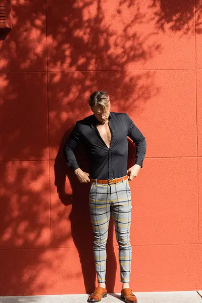 Un bel homme sexy pose dans une tenue élégante contre un mur rouge — Photo de stock