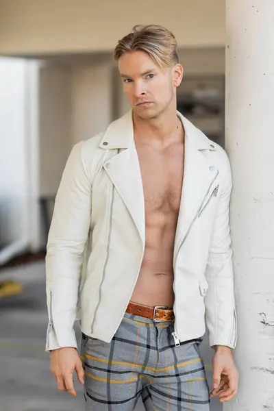 A handsome blonde man poses in a white leather jacket and plaid pants on a street in Florida. — Stock Photo