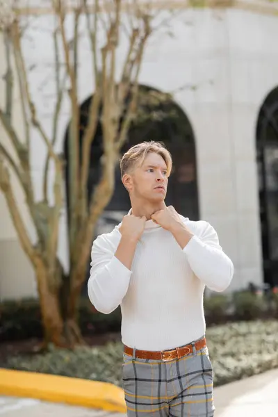 Ein blonder Mann passt sein weißes Hemd an, während er auf einer Straße in Florida posiert. — Stockfoto