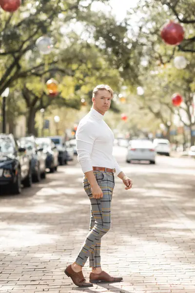 Ein blonder Mann in weißem Hemd und karierter Hose posiert auf einer von Bäumen gesäumten Straße in Florida. — Stockfoto