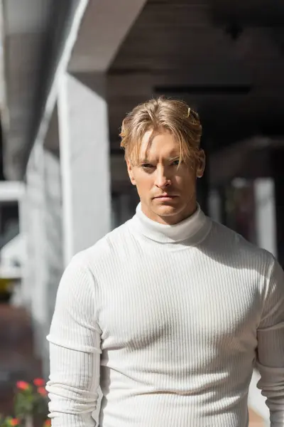 A blonde man poses in a white turtleneck sweater on a street in Florida. — Stock Photo