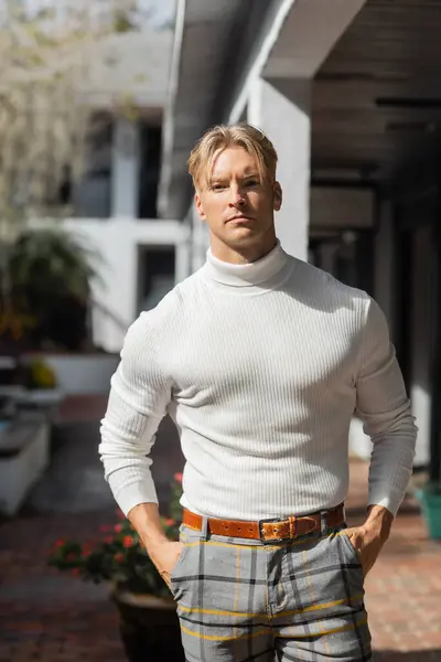 A blonde man poses on a street in Florida, wearing a white turtleneck sweater and plaid pants. — Stock Photo