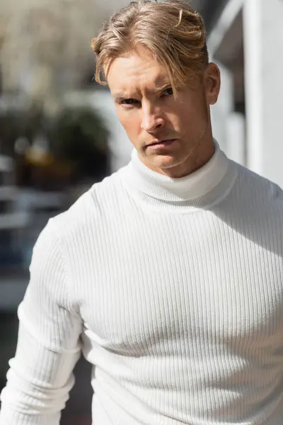 Un bel homme blond au col roulé blanc pose sur une rue ensoleillée de Floride. — Photo de stock