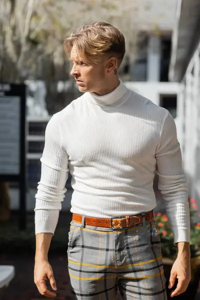 A handsome blonde man poses in a white turtleneck and plaid pants on a Florida street. — Stock Photo