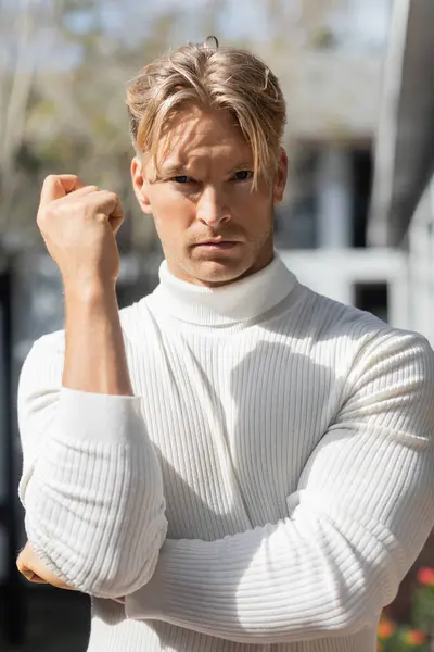 A handsome blonde man in a white turtleneck sweater poses on a street in Florida. — Stock Photo