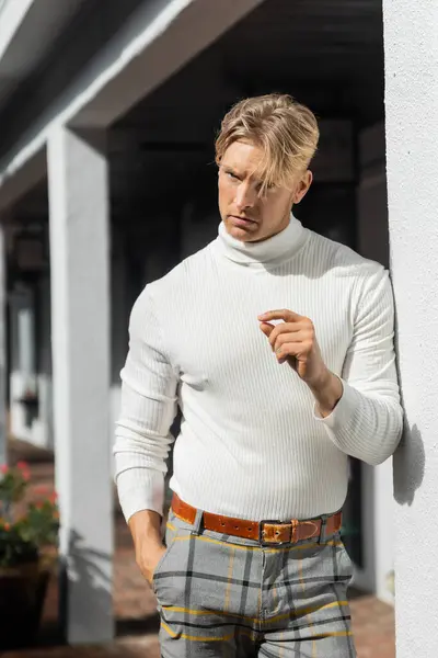 Un hombre rubio posa casualmente con un cuello alto blanco y pantalones a cuadros en un patio de Florida. - foto de stock