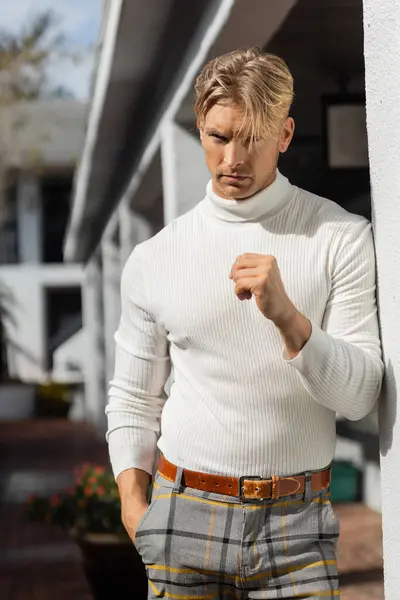 A blonde man in a white turtleneck and plaid pants poses against a white wall in a Florida neighborhood. — Stock Photo