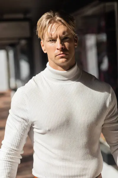 A handsome blonde man poses in a white turtleneck on a Florida street, bathed in the warm afternoon sunlight. — Stock Photo