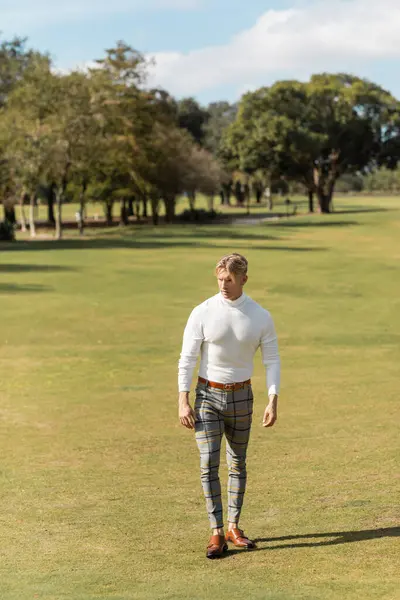 Un uomo biondo in abiti eleganti passeggia in un parco verde a Miami. — Foto stock