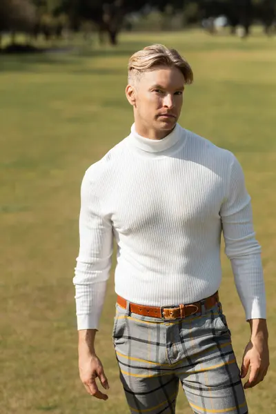 Blonde man in stylish attire walking in a green park in Miami. — Stock Photo