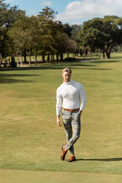 Un uomo biondo in abiti eleganti passeggia in un parco verde a Miami. — Foto stock