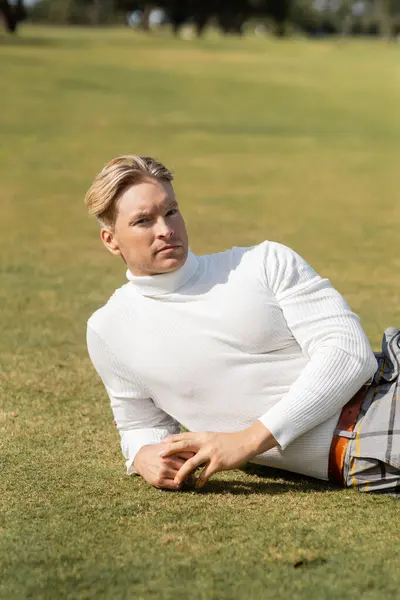 Un uomo biondo in abiti eleganti giace in un parco verde a Miami. — Foto stock