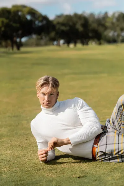 Un uomo biondo in abiti eleganti posa sull'erba in un parco di Miami. — Foto stock