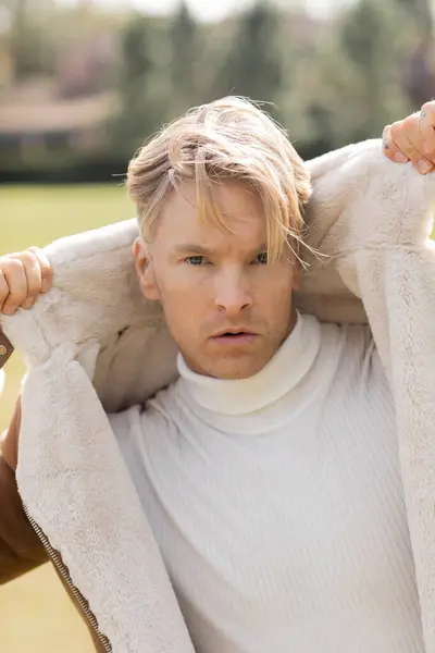 A blonde man in a stylish white turtleneck in a green park — Stock Photo