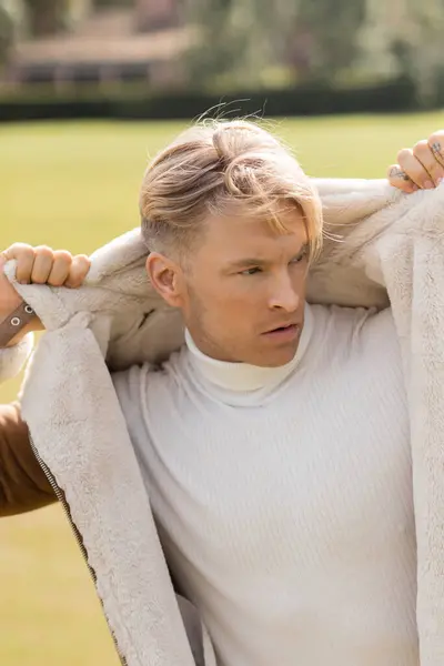 Ein hübscher blonder Mann in stylischer Kleidung geht durch einen grünen Park — Stockfoto