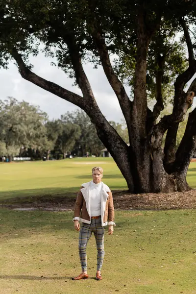 A blonde man in stylish attire walks through a green park in Miami. — Stock Photo