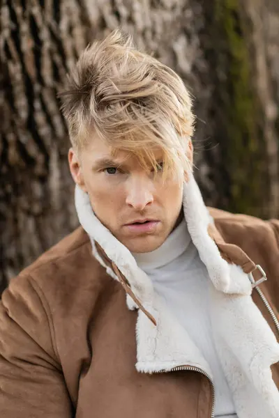 A blonde man in a stylish brown jacket walks through a green park in Miami. — Stock Photo