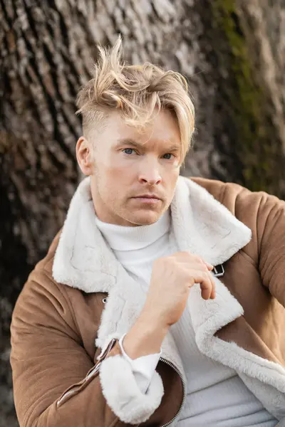 A handsome blonde man in a stylish jacket walks through a green park in Miami. — Stock Photo