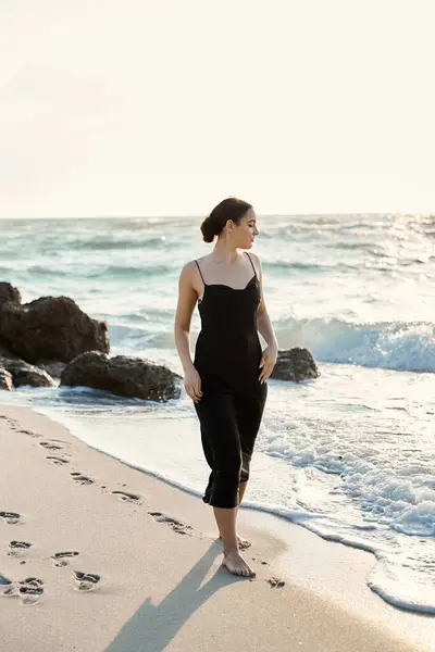 A young woman in a black sundress walks along the shoreline of Miami Beach, leaving footprints in the sand. — Stock Photo