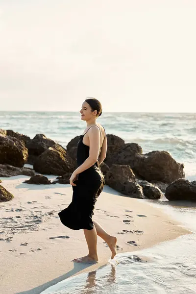 A woman in a black dress walks along the sandy beach in Miami, Florida, with the setting sun casting a warm glow on the scene. — Stock Photo