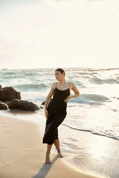 A young woman in a black sundress strolls along the sandy shore of Miami Beach, enjoying the warm evening sun and the gentle sea breeze. — Stock Photo