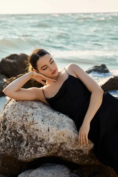 A young woman in a black sundress rests on a rock, taking in the serene beauty of the Miami Beach coastline. — Stock Photo
