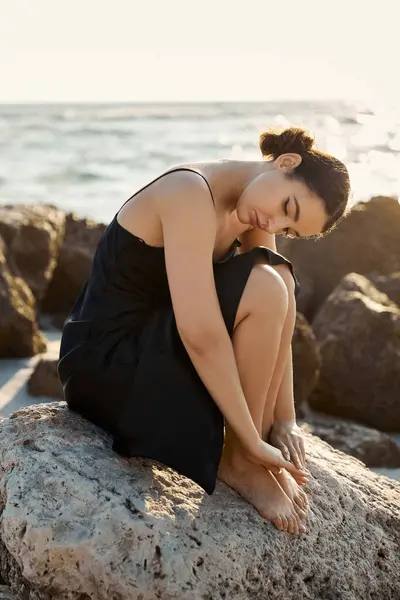 A woman in a black sundress sits on a rock on a Miami Beach shore, bathed in the soft glow of a setting sun. — Stock Photo
