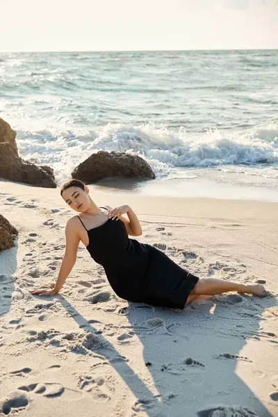 A young woman in a black sundress relaxes on the beach in Miami, Florida, with the ocean waves crashing in the background. — Stock Photo