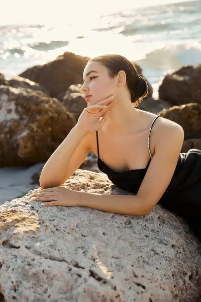 A young woman in a black sundress rests on a rock on Miami Beach, gazing out at the ocean. — Stock Photo
