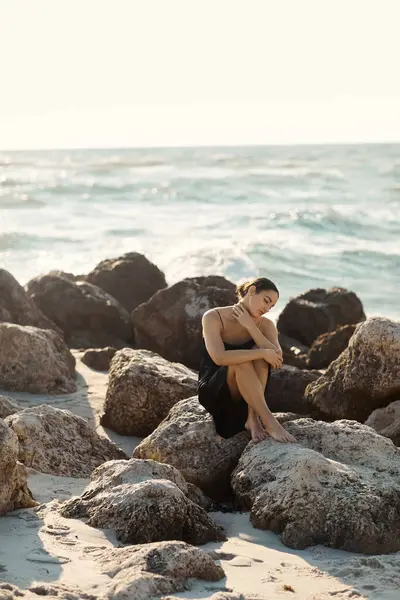 A young woman sits on a large rock on Miami Beach, wearing a black sundress — Stock Photo