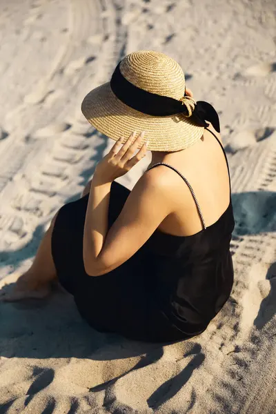 A woman in a black sundress and a straw hat relaxes on Miami Beach, enjoying the golden glow of the setting sun. — Stock Photo