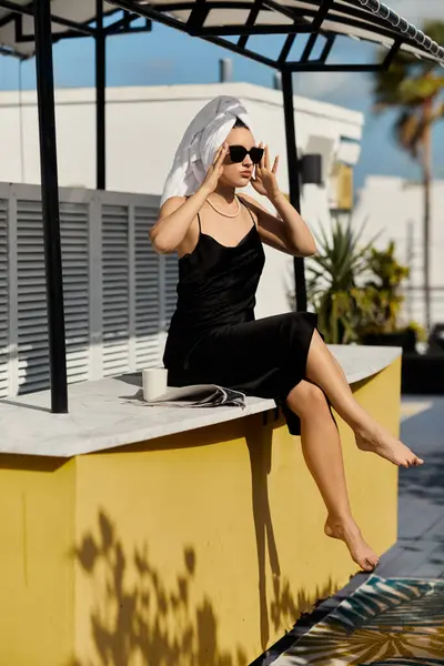 A stylish woman in a black slip dress and sunglasses relaxes by the pool, taking in the Miami sun. — Stock Photo