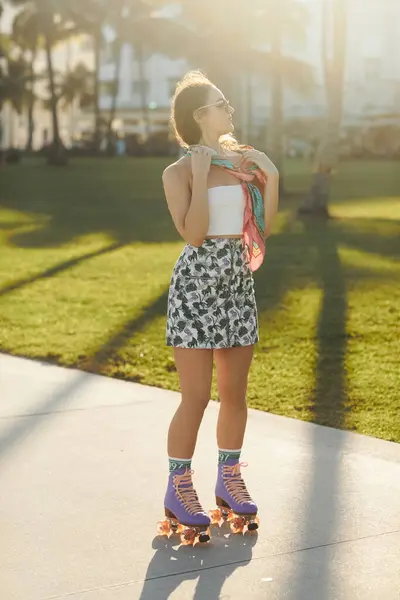 A young woman in sunglasses and a stylish skirt rollerblades on the sidewalk in Miami at sunset. — Stock Photo
