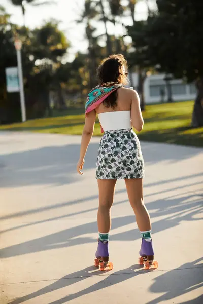 A young woman in sunglasses and a stylish outfit skates down a Miami street. — Stock Photo