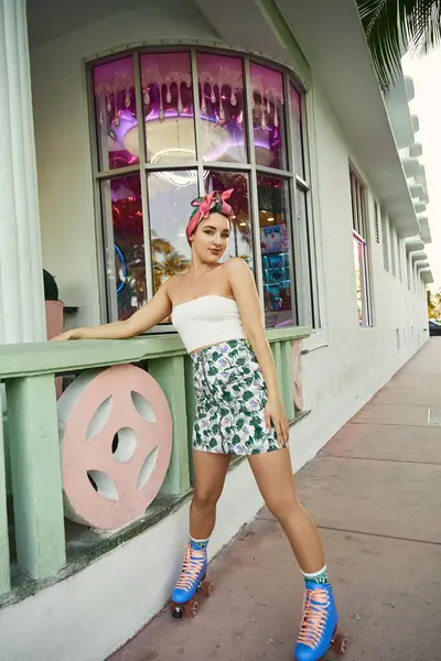Une jeune femme aux lunettes de soleil et aux vêtements élégants skate devant un bâtiment rose et vert à Miami. — Photo de stock