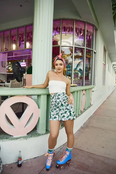 Une jeune femme en lunettes de soleil et une jupe florale patinent devant une devanture d'inspiration vintage à Miami. — Photo de stock