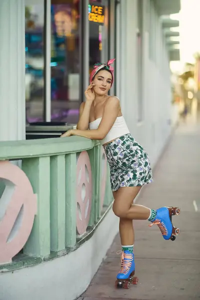 Une jeune femme élégante en lunettes de soleil se penche contre une rampe, un patin à roulettes levé, à Miami. — Photo de stock