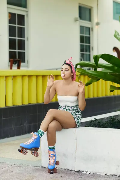 Una giovane donna in occhiali da sole e abbigliamento elegante soffia una bolla mentre è seduta su un marciapiede a Miami, indossando pattini a rotelle. — Foto stock