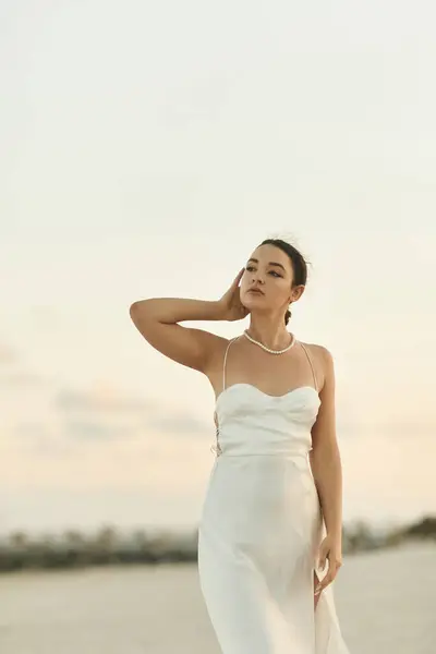 A young woman in a white dress, with her hair pulled back, stands on a sandy beach in Miami as the sun sets. — Stock Photo